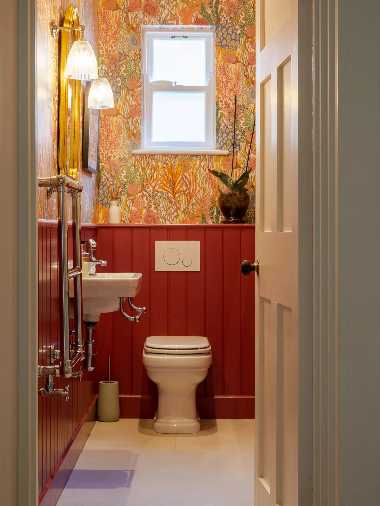 Red-panelled cloakroom with patterned wallpaper, a white basin and toilet