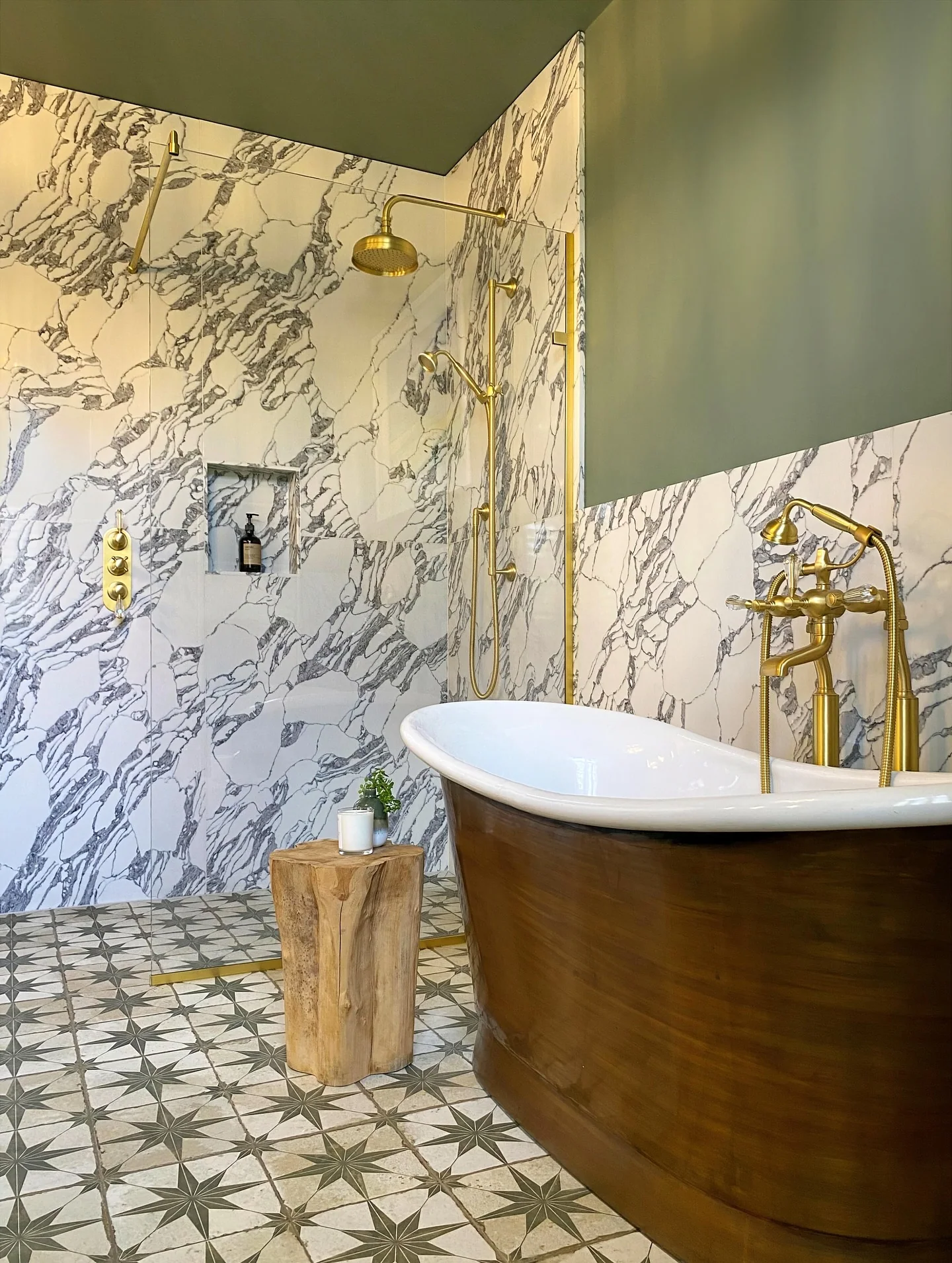 Freestanding bath with a brass filler beside veined marble-patterned walls