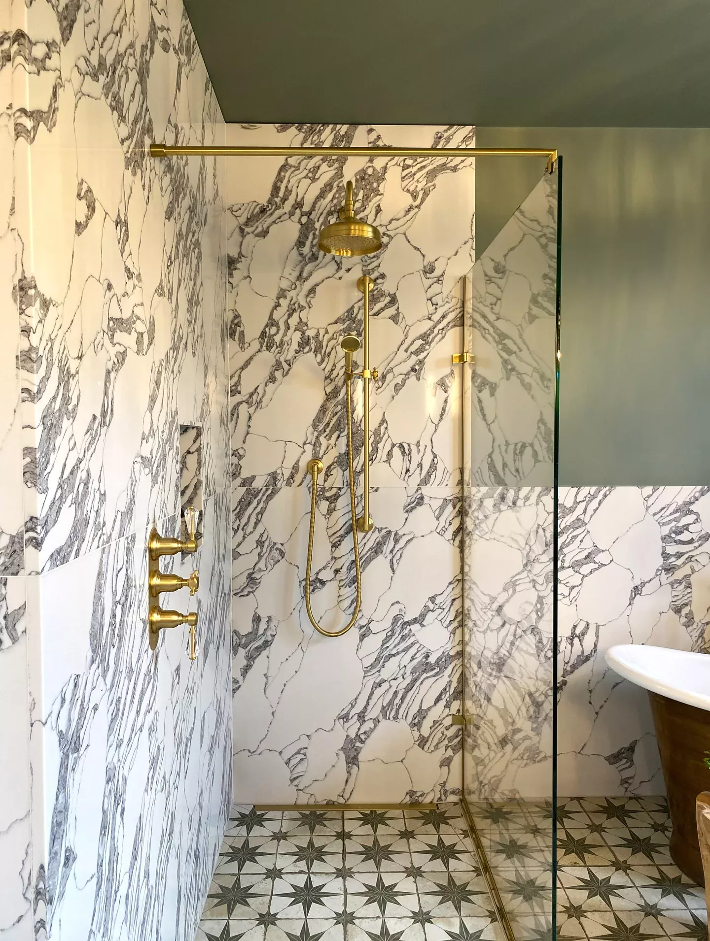 Glass walk-in shower with brass fittings and marble-patterned walls