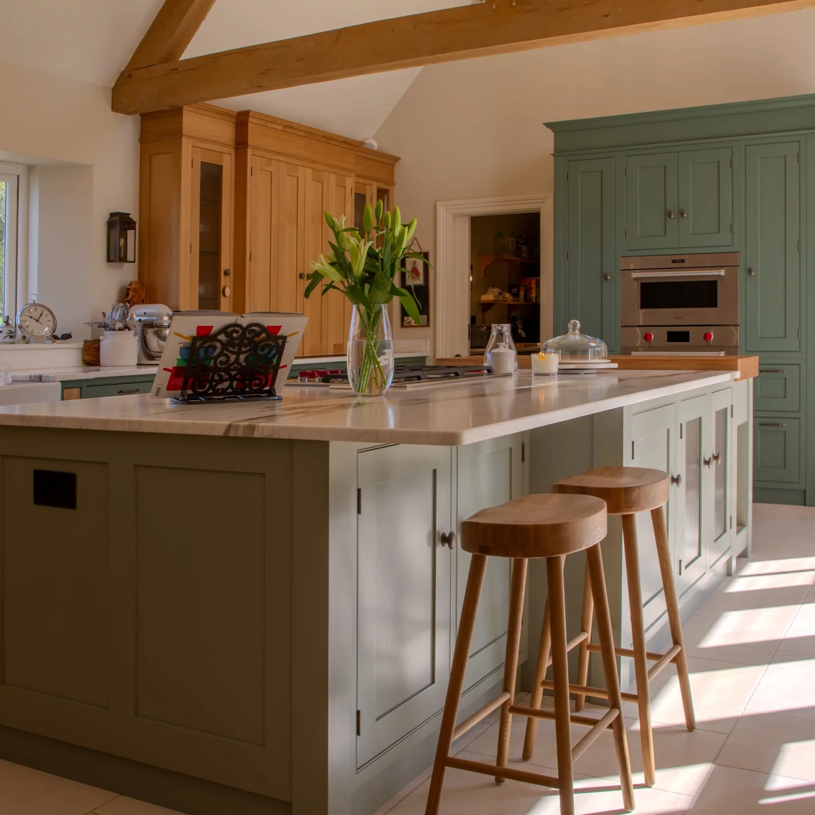 Green kitchen island with timber stools beneath exposed oak beams