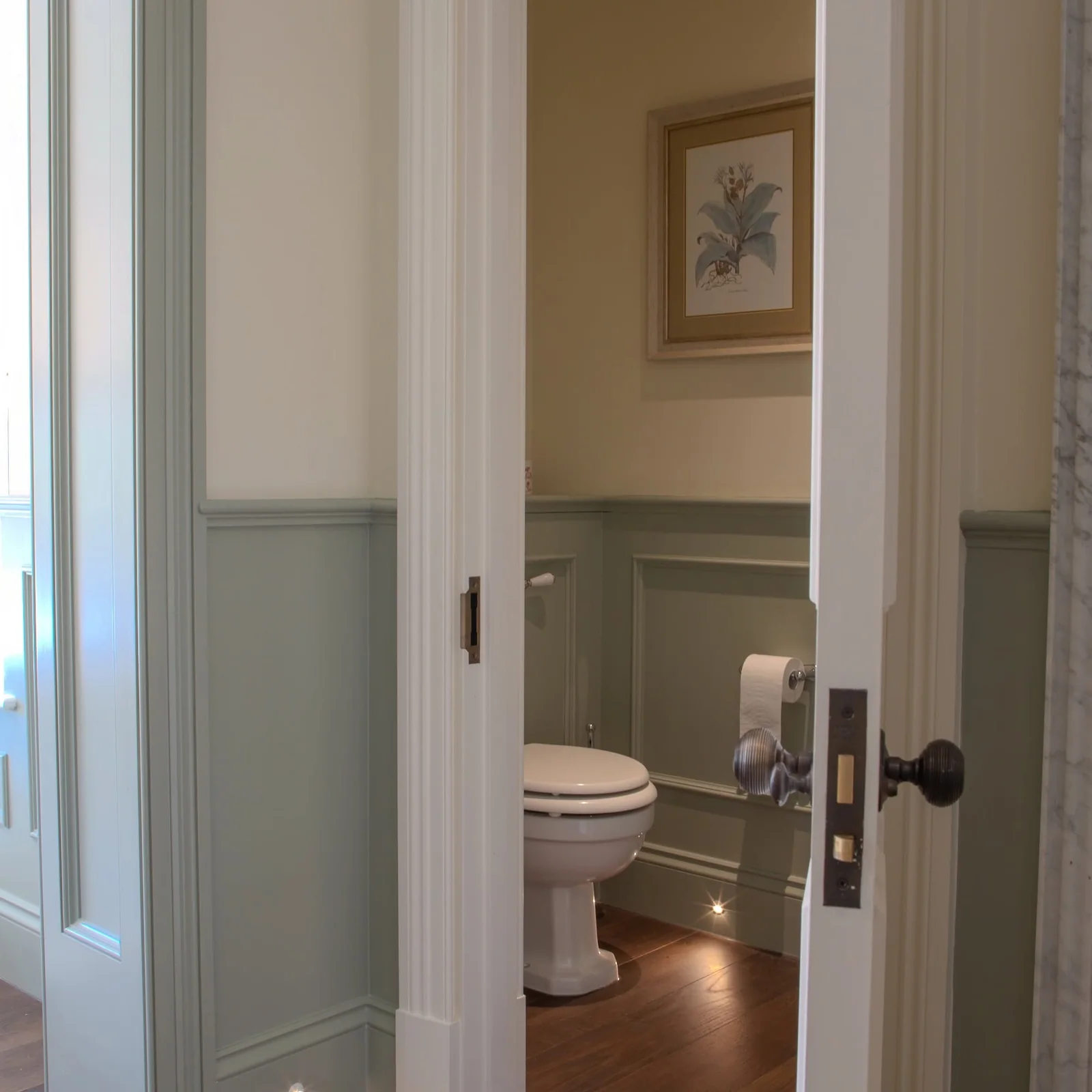 Toilet and basin in a panelled cloakroom viewed through an open doorway