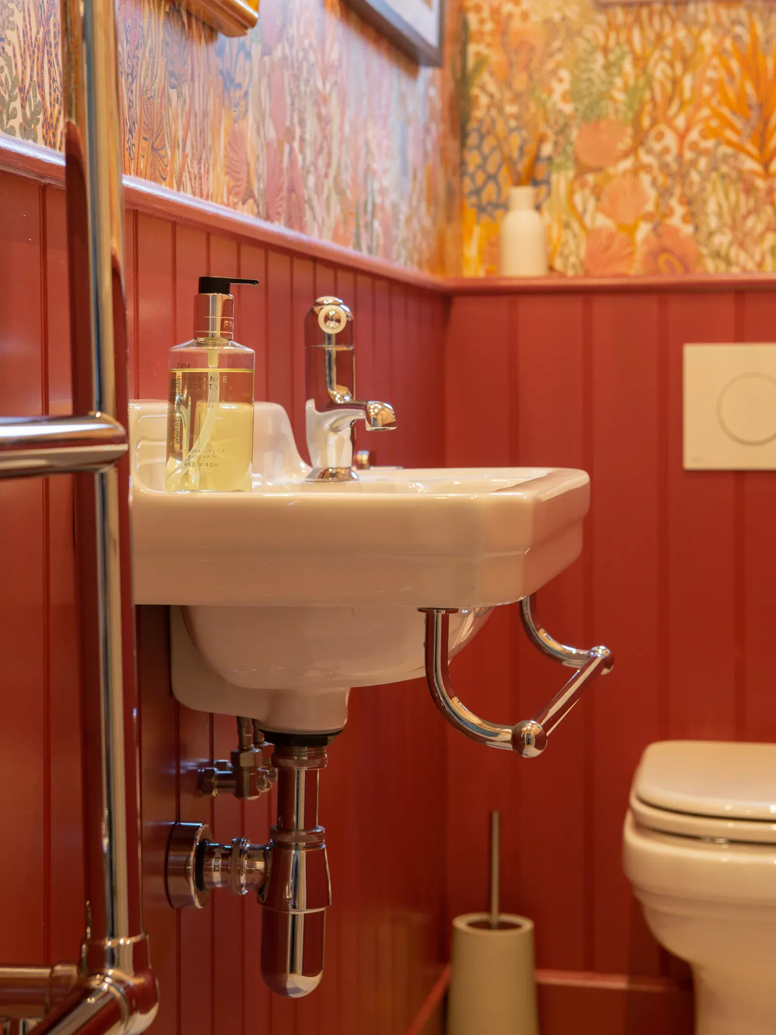 White wall-mounted basin against red panelling and patterned wallpaper