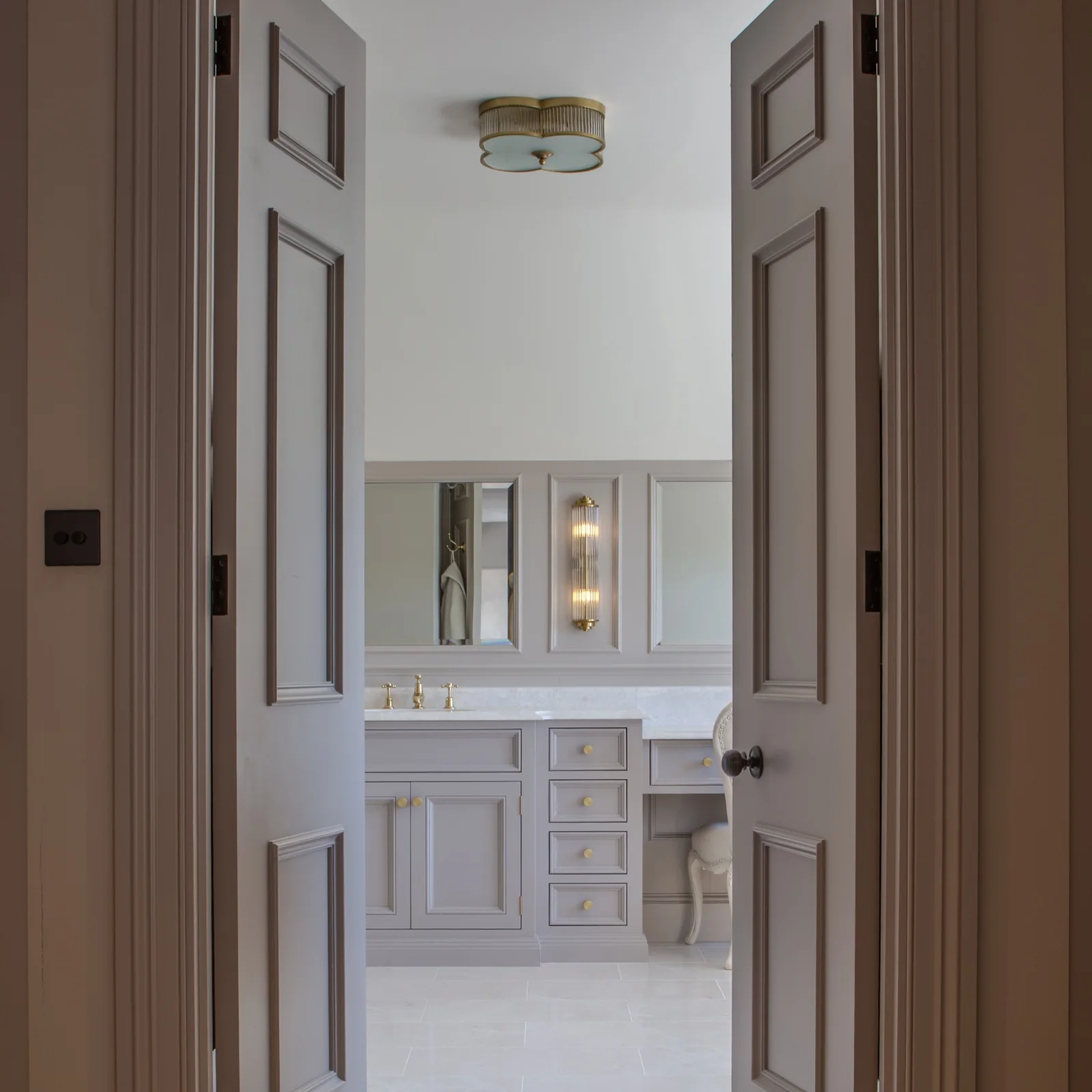 Pale bathroom vanity and mirrored wall seen through a doorway