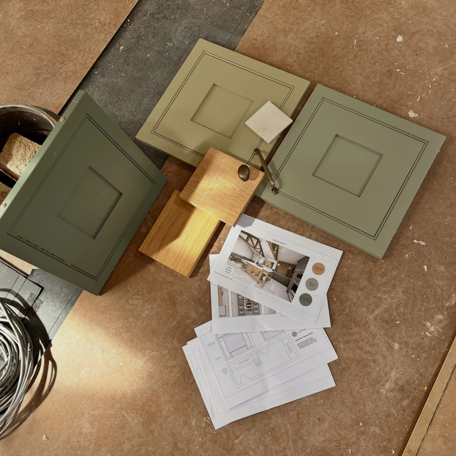 Green cabinet door samples, timber finishes and kitchen plans compared during the design process