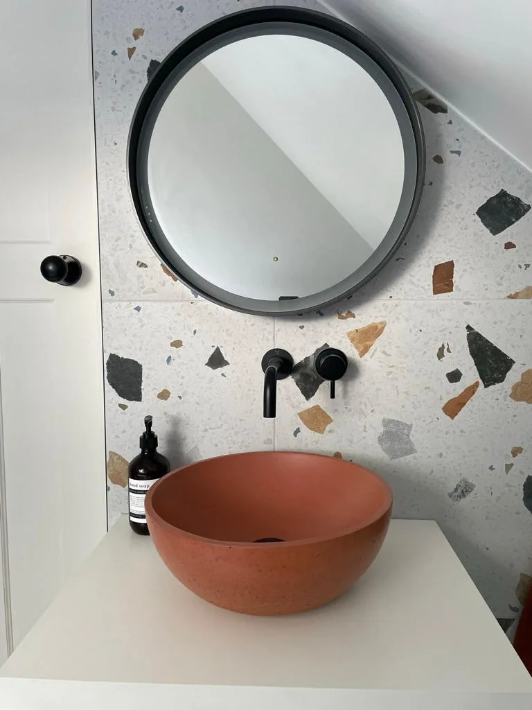 Amber basin and circular mirror against a terrazzo bathroom wall